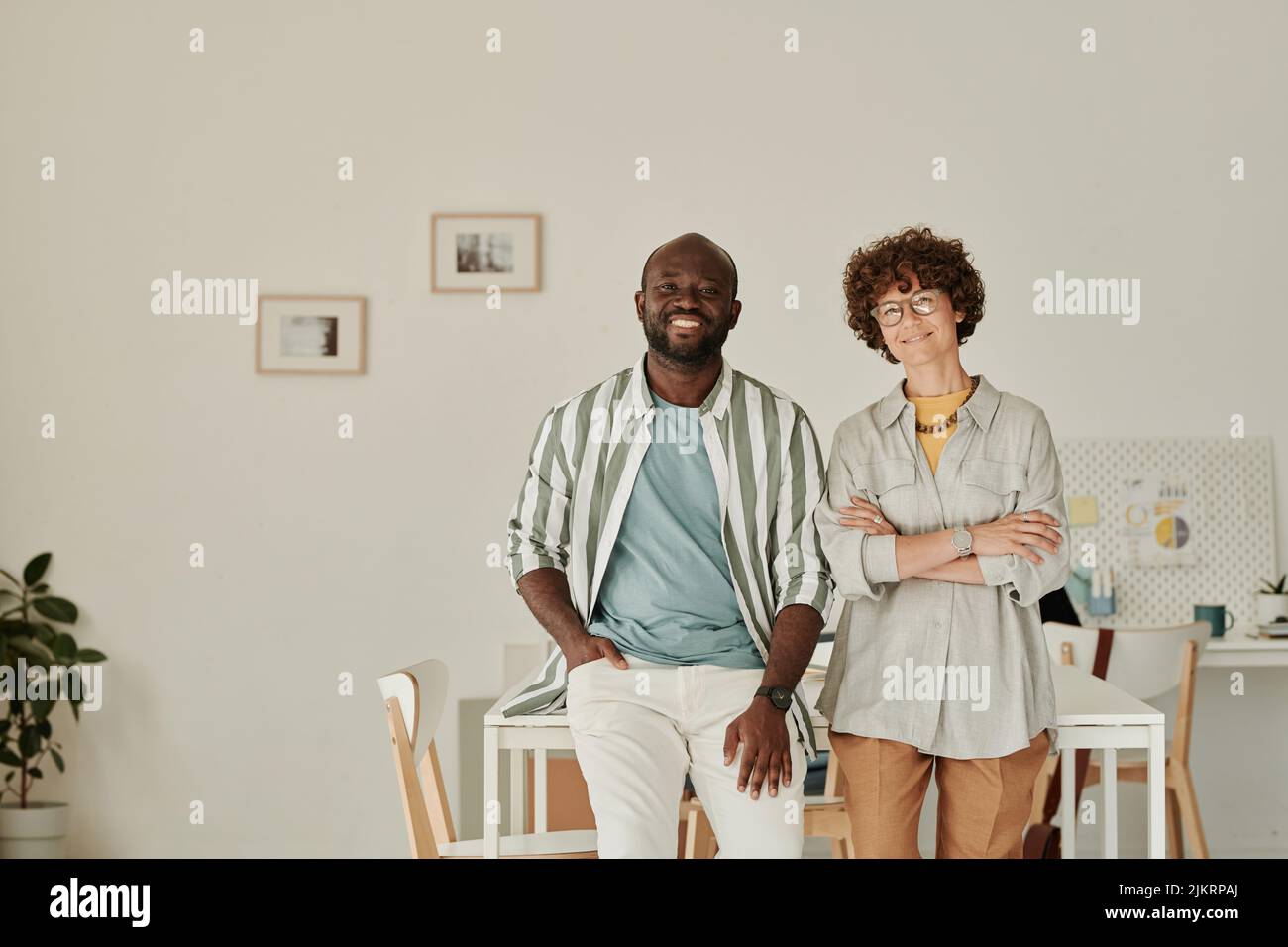 Ritratto di giovani colleghi di successo che sorridono alla fotocamera mentre sono in piedi insieme in ufficio Foto Stock