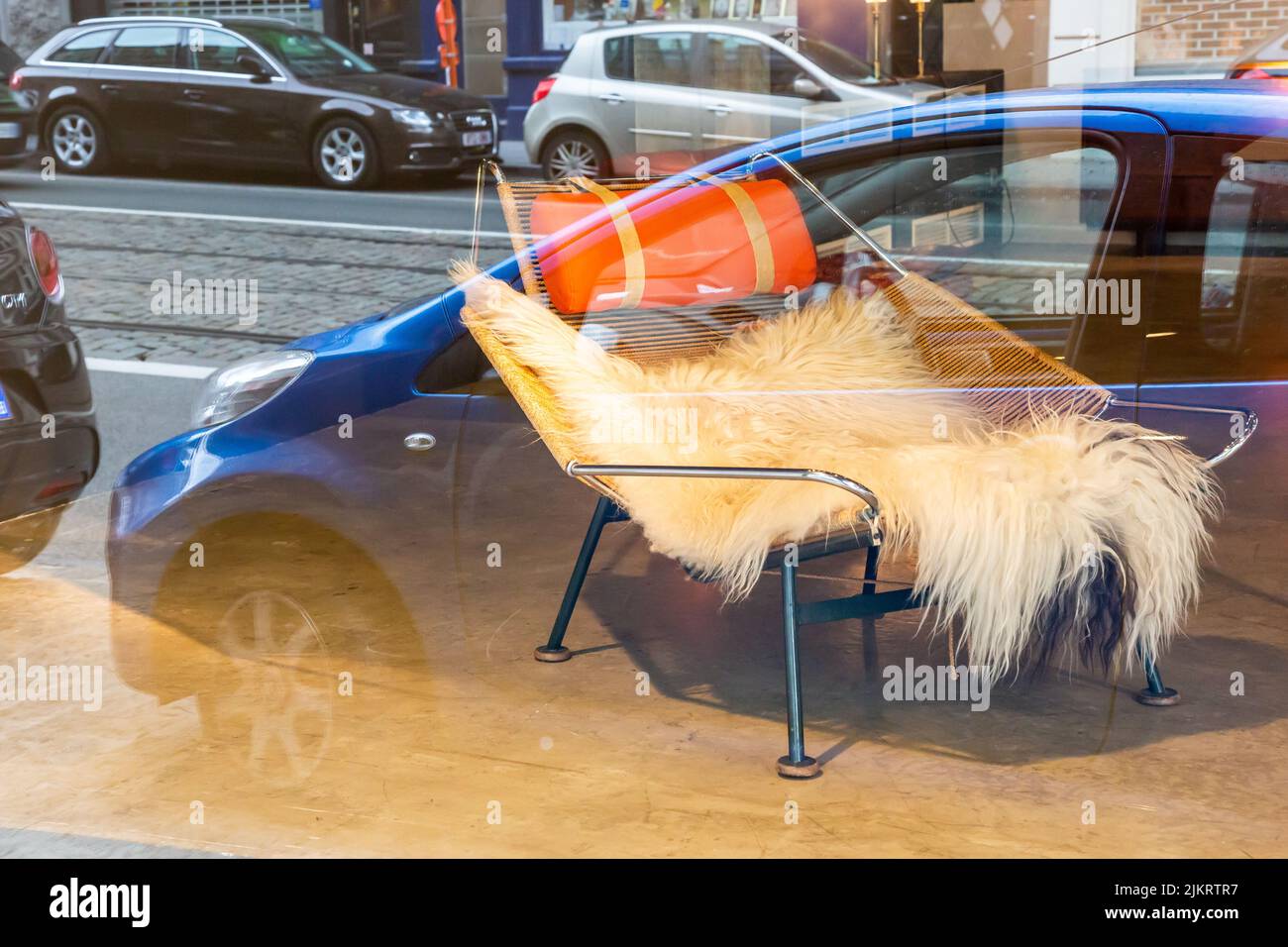 Riflesso in una vetrina: Auto parcheggiate e una poltrona in vendita, ricoperta di pelle animale. Foto Stock