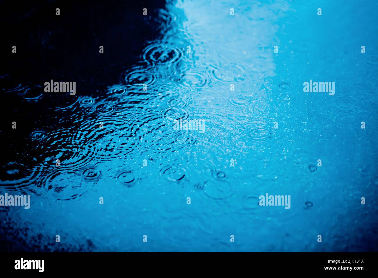 Le gocce di pioggia cadono sulla superficie dell'acqua di una pozza profonda in città sull'asfalto. Maltempo. Acqua. Foto Stock