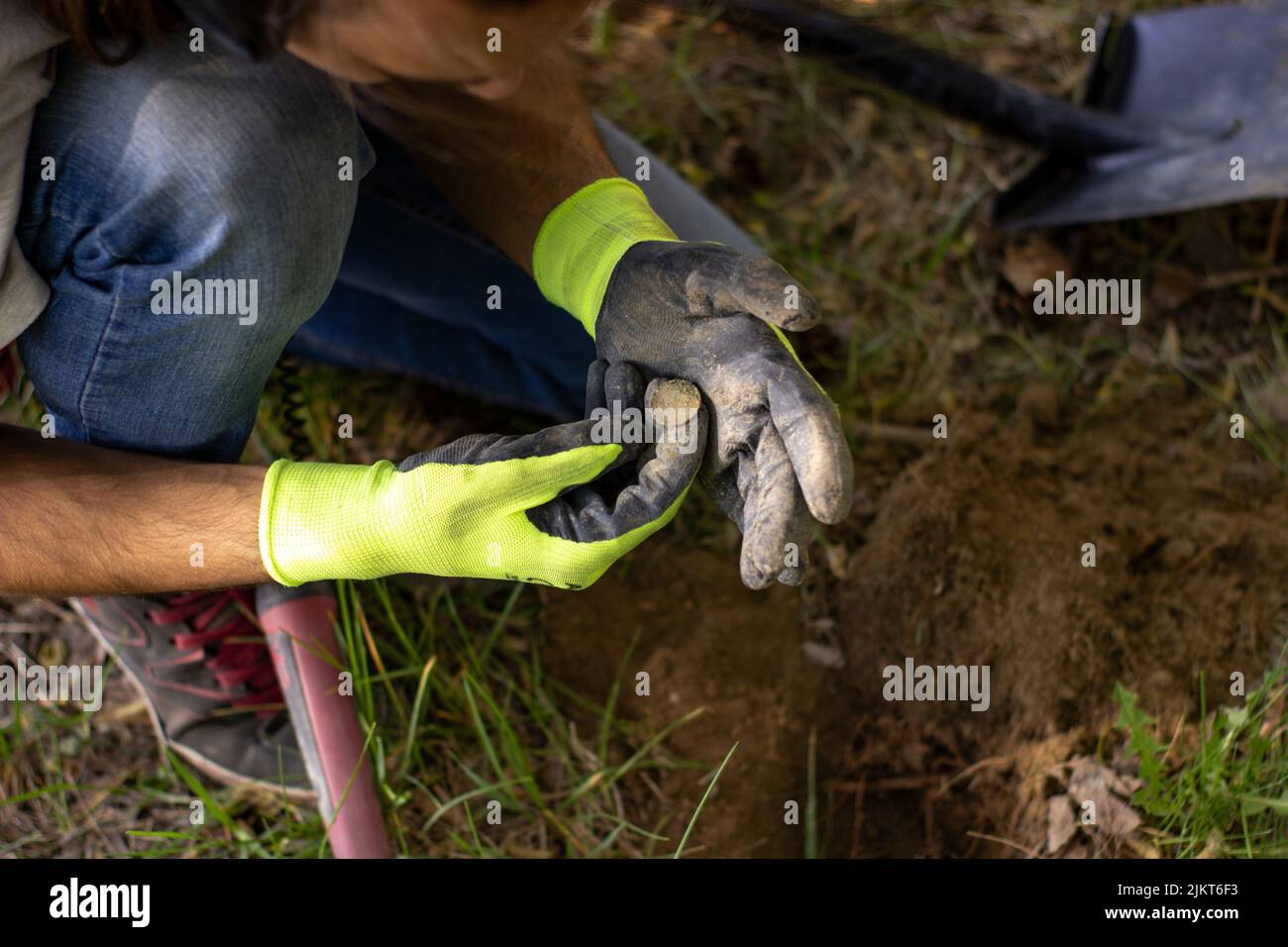 un uomo in guanti è alla ricerca di un tesoro nel terreno con l'aiuto di un pinpointer nella foresta di primavera. pala di fronte Foto Stock