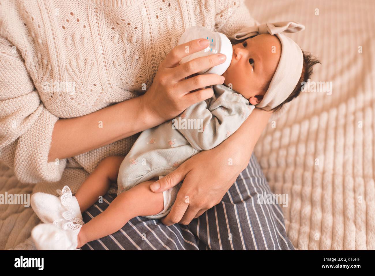 Madre che allatta bambino bambina con latte in bottiglia indossare abiti casual in camera da letto closeup. Maternità. Maternità. Alimentazione sana mangiando. Foto Stock