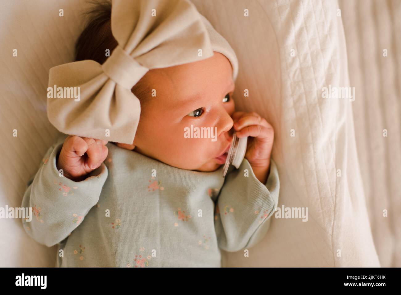 Carina bambina neonato svegliarsi indossare archetto ad arco e pigiami con succhietto in vista sul letto. Infanzia. Buongiorno. Foto Stock