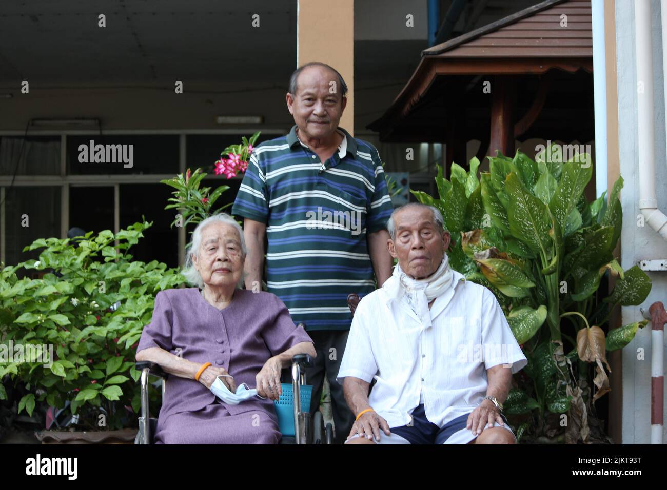 Un maschio dell'Asia orientale che si trova dietro i suoi vecchi genitori seduti in giardino Foto Stock