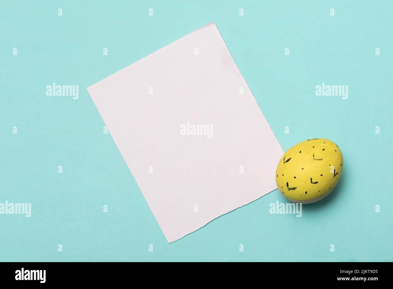 Un primo piano di un uovo di Pasqua con carta bianca isolato su sfondo azzurro con spazio copia Foto Stock