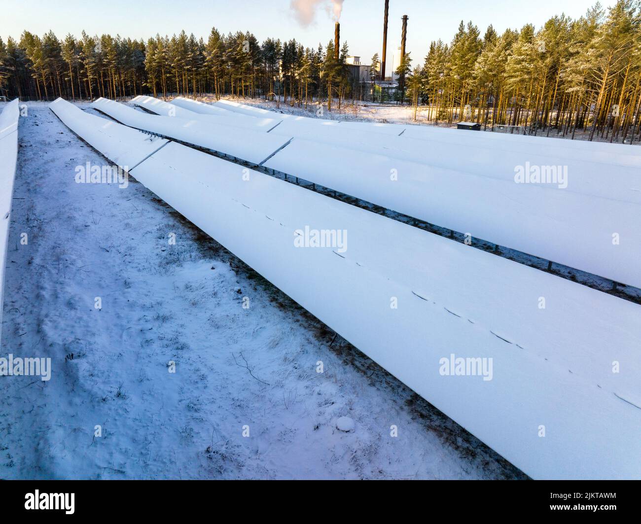 Vista aerea intorno a un campo di pannelli solari innevati con sfondo di fabbrica Foto Stock