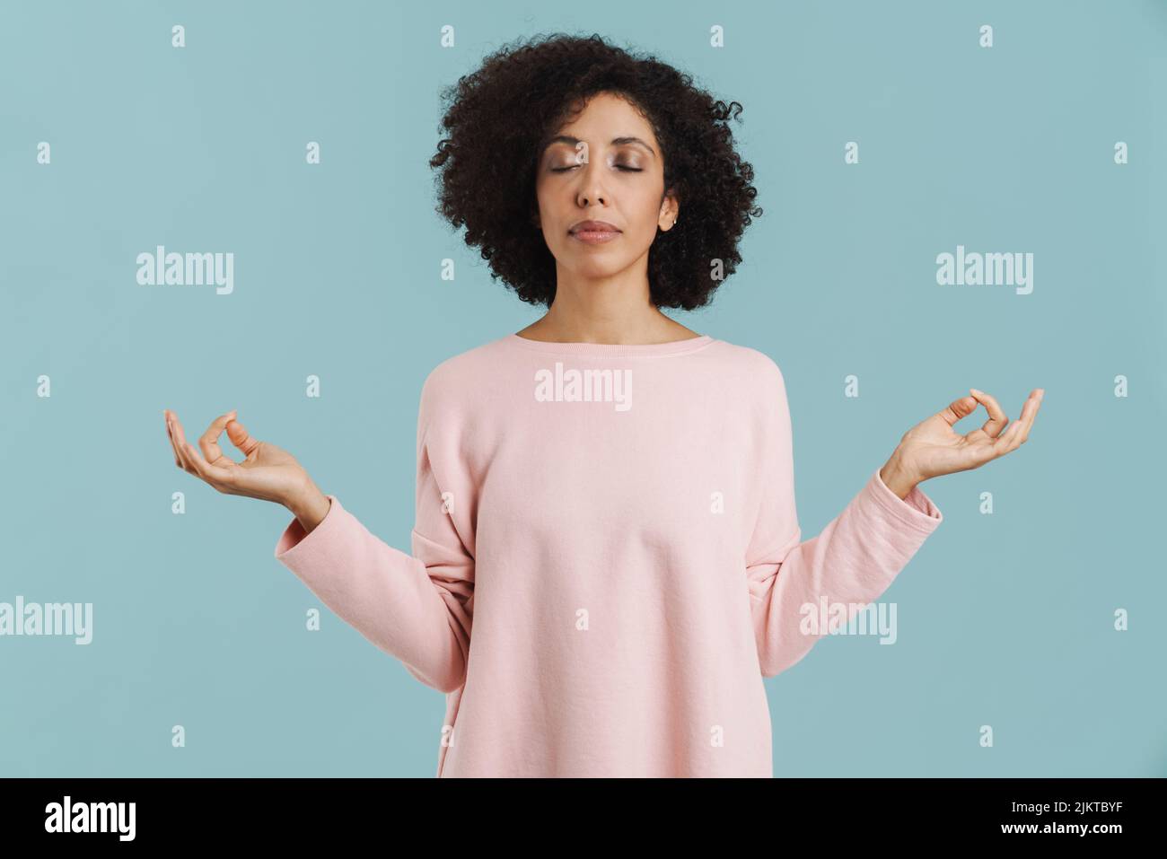 Giovane donna nera pacifica meditating con gli occhi chiusi isolato su sfondo blu Foto Stock
