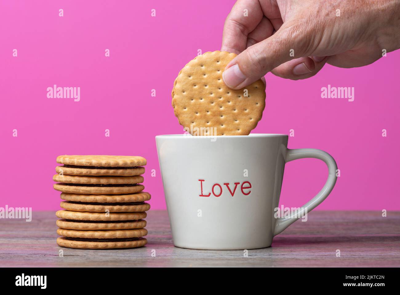 Mano che si stende un biscotto in una tazza con 'Amore' scritto su di esso. Foto Stock