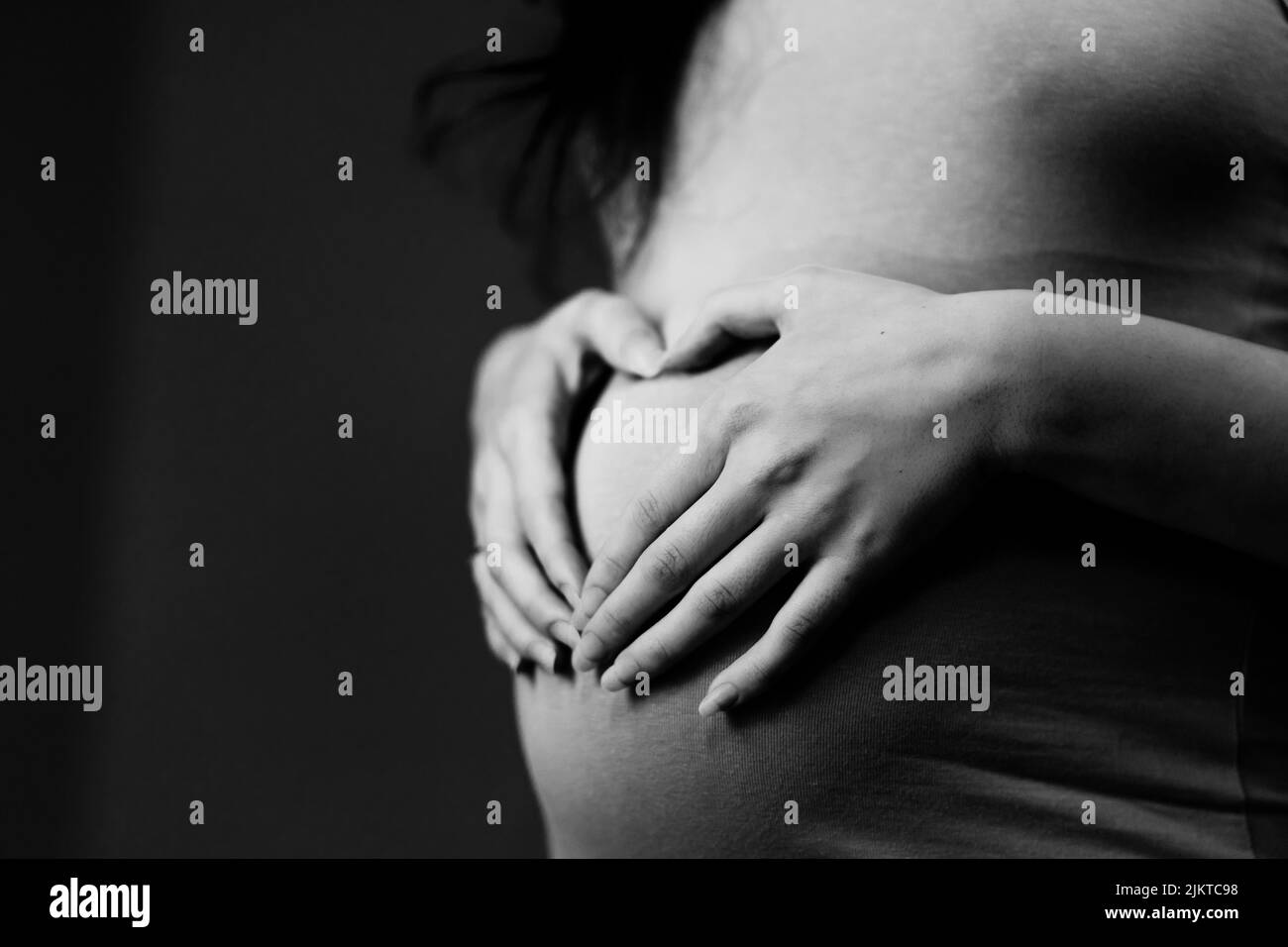 Donna incinta che fa un cuore sul suo ventre Foto Stock