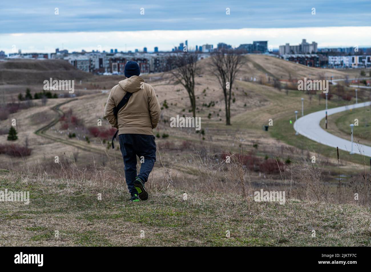 Un maschio da dietro che indossa un cappello nero che scende giù per la collina coperta di erba Foto Stock