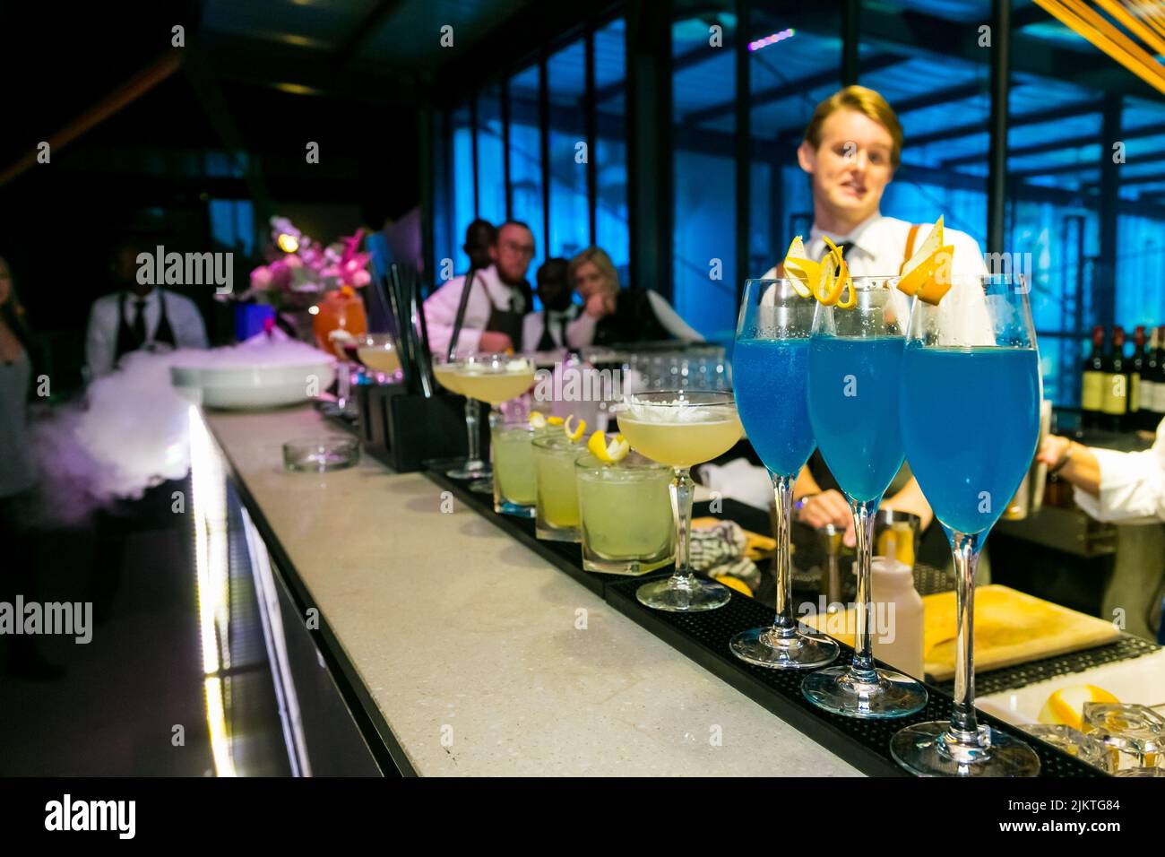 Bevande colorate sul banco del bar con barman sullo sfondo durante un evento al coperto a Johannesburg Foto Stock