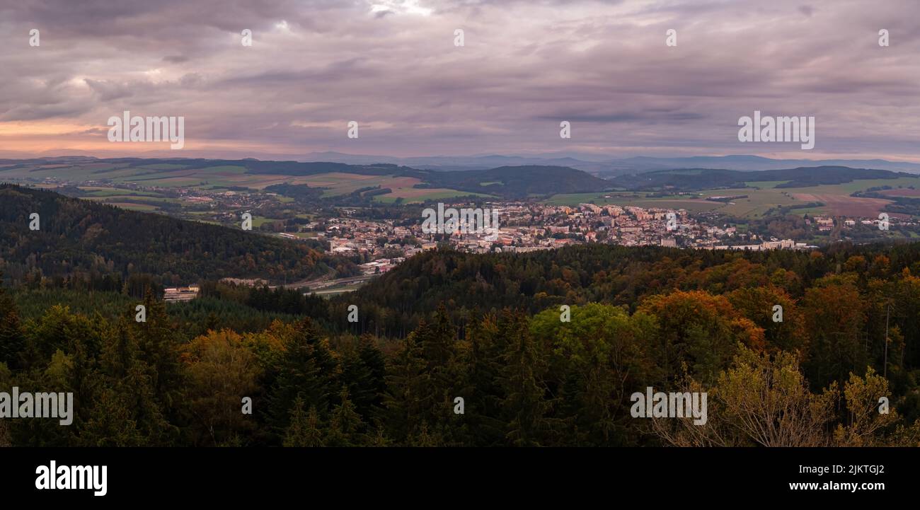 Una vista panoramica di una città circondata da verdi montagne al tramonto nuvoloso Foto Stock