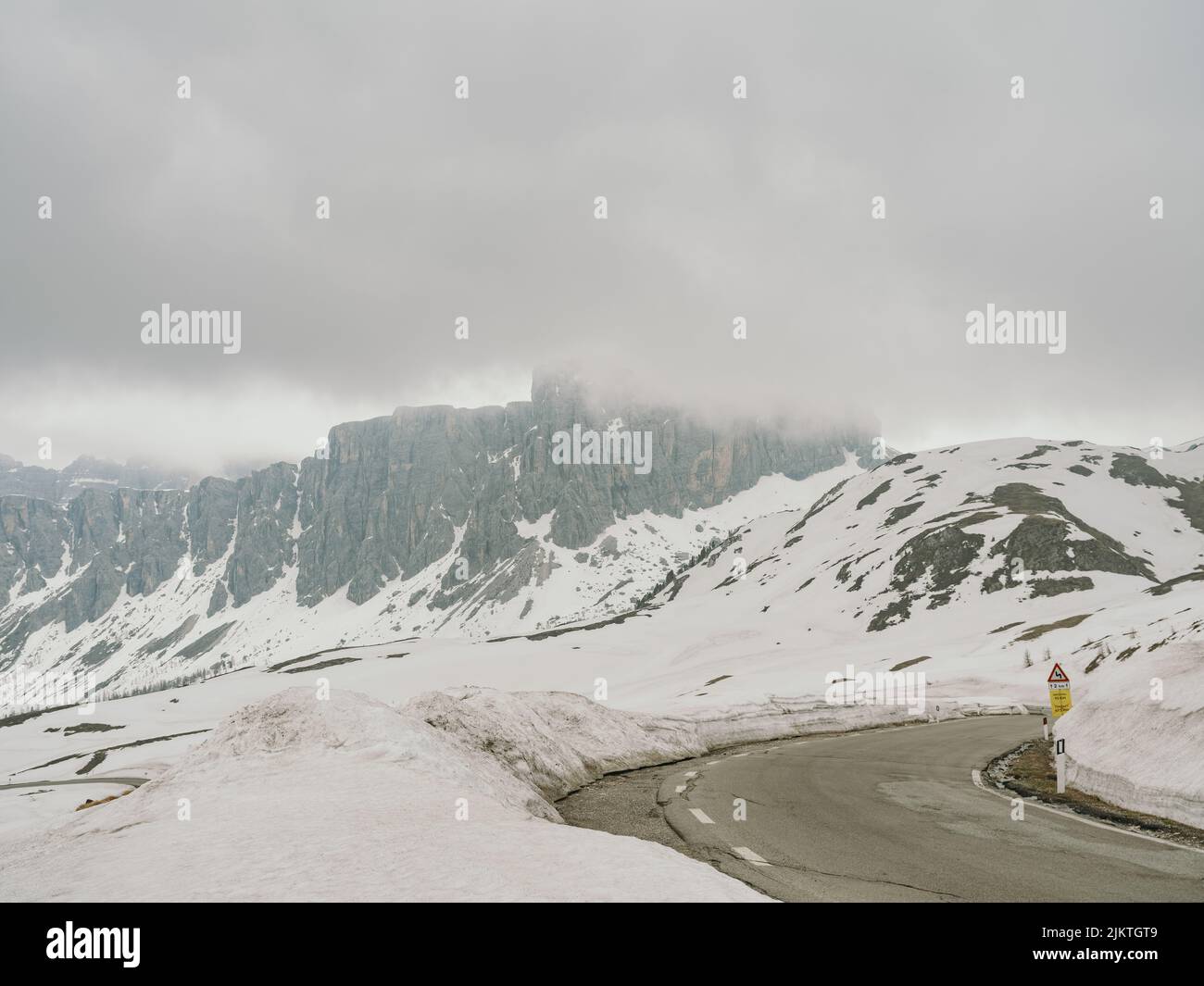 Un bellissimo scatto di un'autostrada circondata da colline completamente innevate sullo sfondo di una scogliera in tempo nebboso. Foto Stock