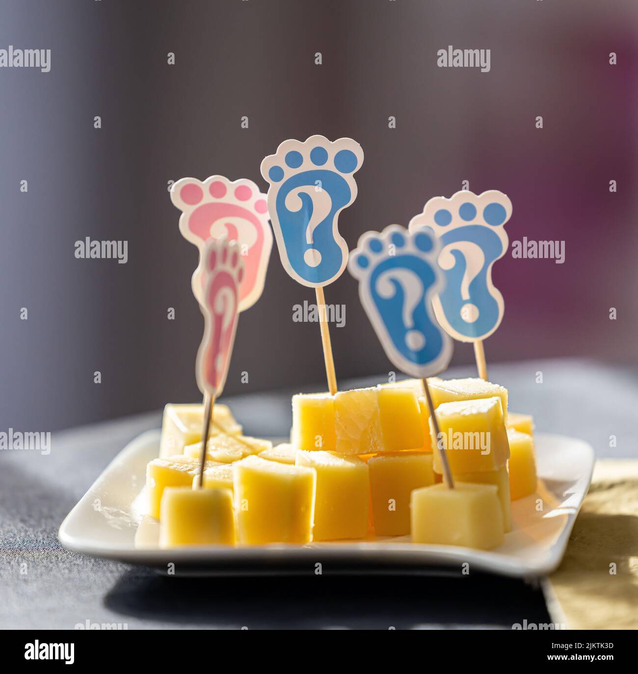 I piedi rosa e blu del bambino attaccano i pezzi di formaggio su un piatto in una festa di rivelazione di genere Foto Stock