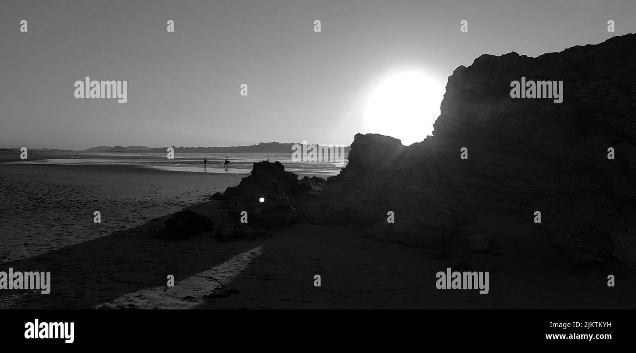 Una scala di grigi di mare o oceano con sole che illumina tutto intorno e rocce massicce in primo piano Foto Stock
