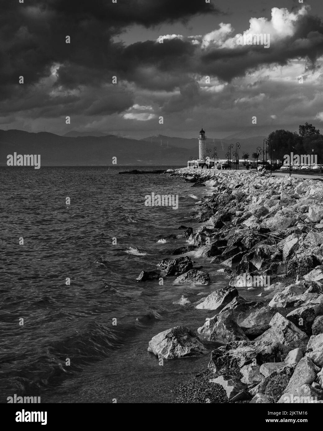 Uno scatto verticale di un litorale roccioso e di un faro in una giornata nuvolosa in bianco e nero Foto Stock