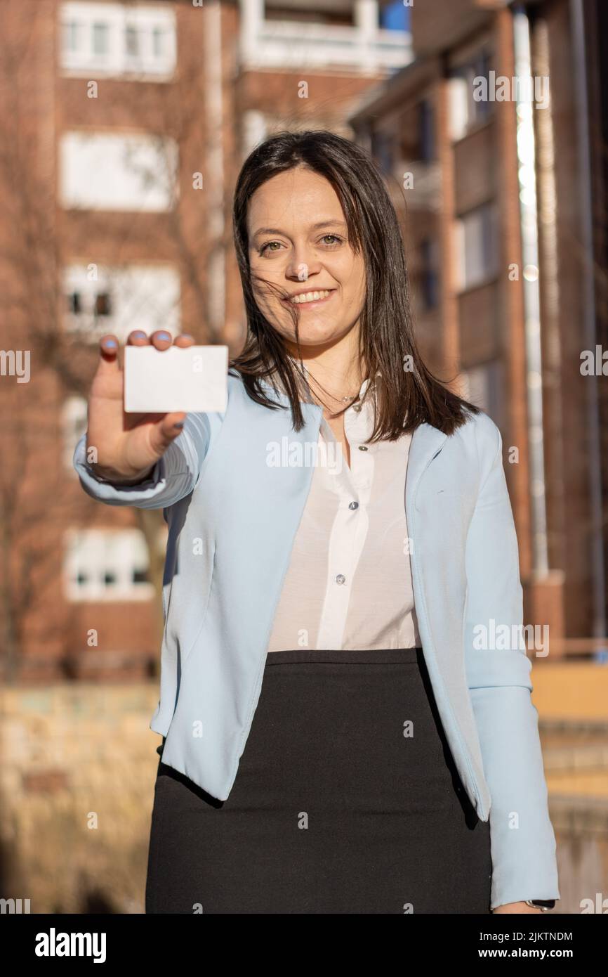 Donna Businesswoman sorridente con giacca blu che mostra il biglietto da visita all'aperto. Verticale. Biglietto da visita Foto Stock