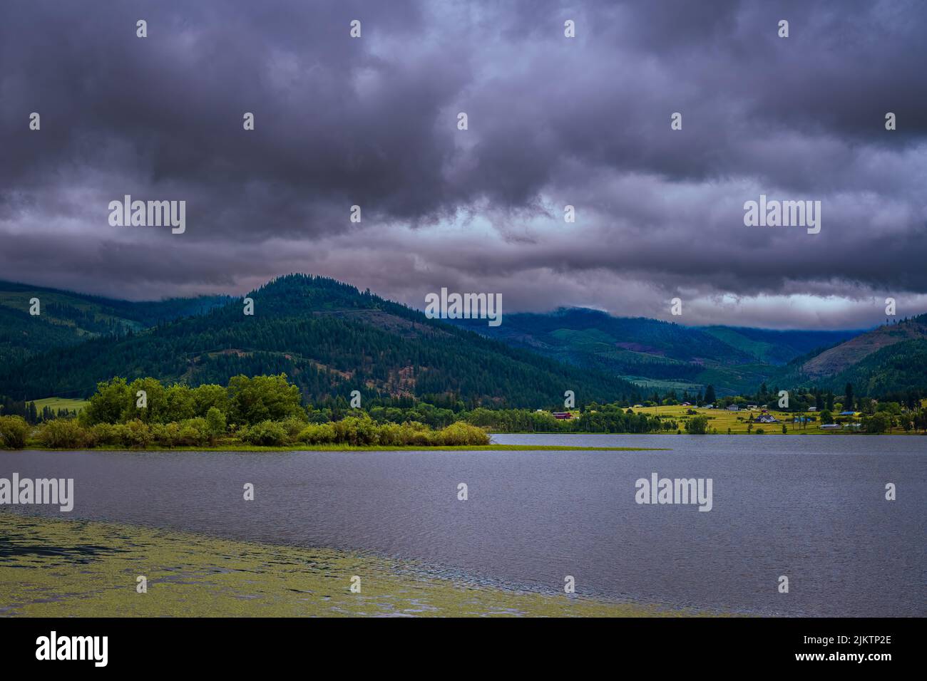 FIUME COUER D'ALENE CON UNA RIVA ALBERATA, MONTAGNE E UN CIELO NUVOLOSO Foto Stock
