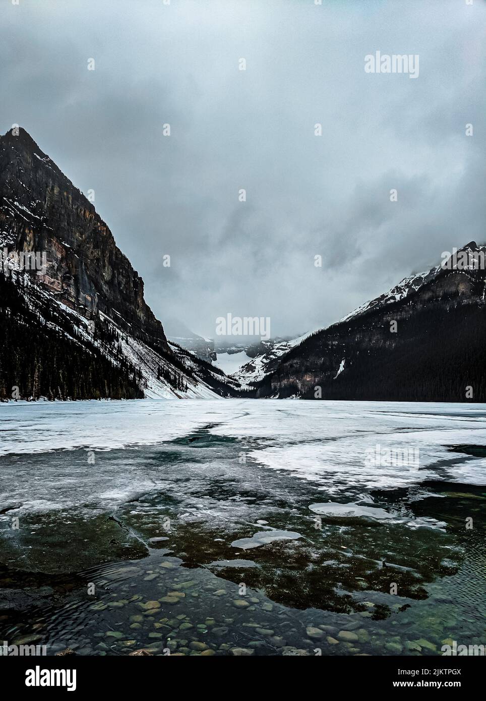 Uno scatto verticale di un fiume che passa attraverso montagne innevate in una fredda e cupa giornata invernale Foto Stock