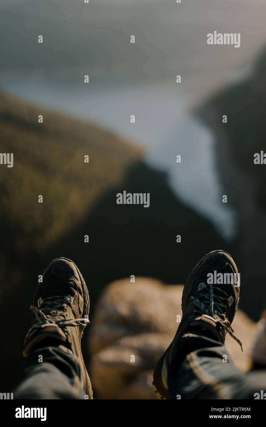 Un'immagine verticale dei piedi di una persona che pende nell'aria sullo sfondo di una valle offuscata e di un lago. Foto Stock