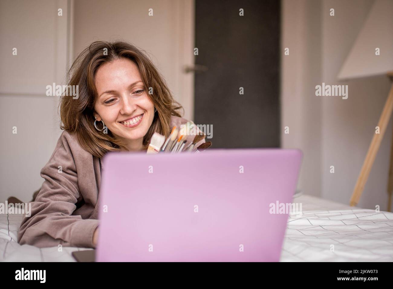 Foto di sorridente studente di pittura con dentifricio e spazzole pronti a prendere la sua classe online e dipingere una tela nella sua stanza Foto Stock