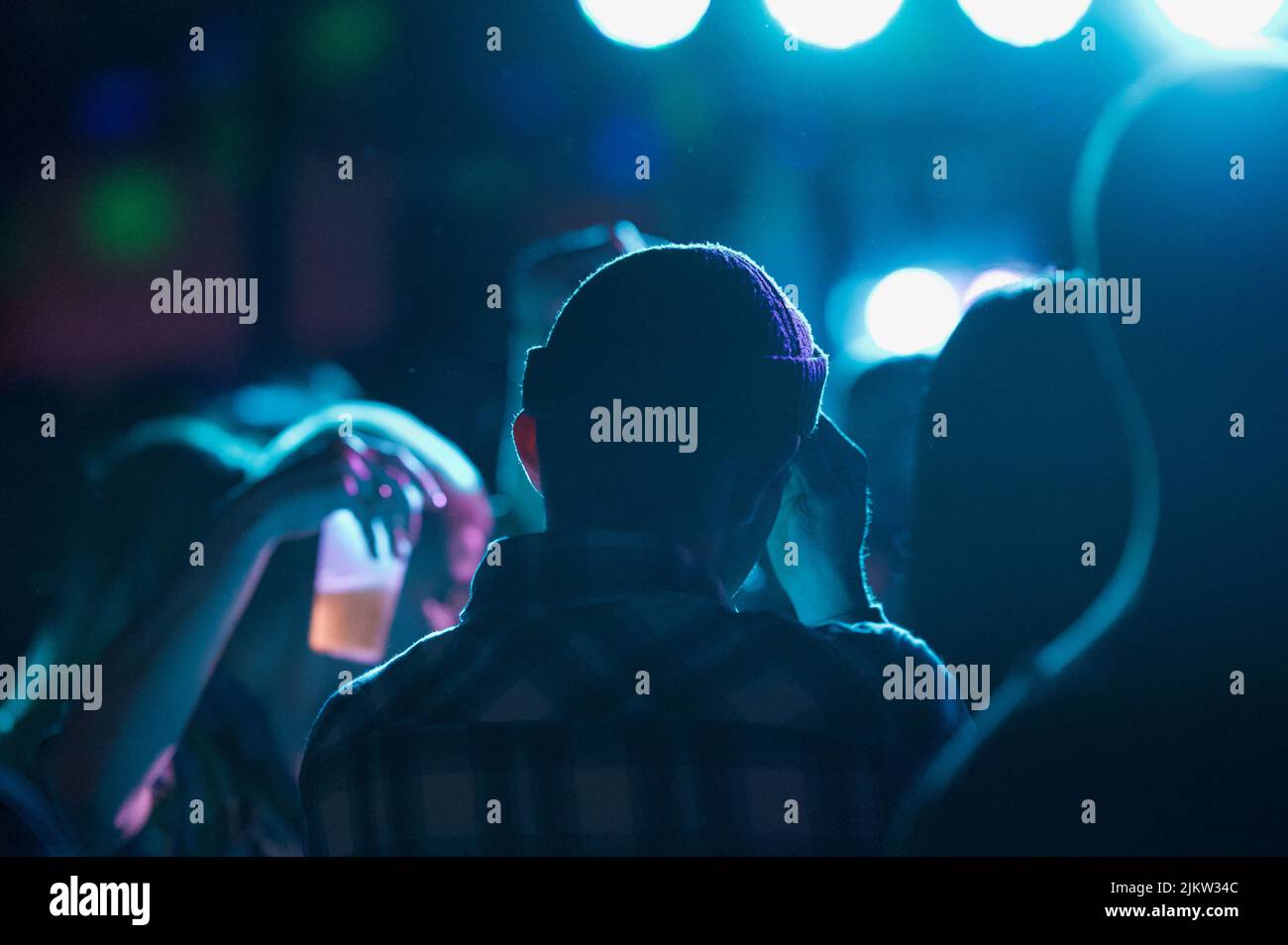 Una vista posteriore di un giovane uomo in un cappello in un randello con le luci blu Foto Stock