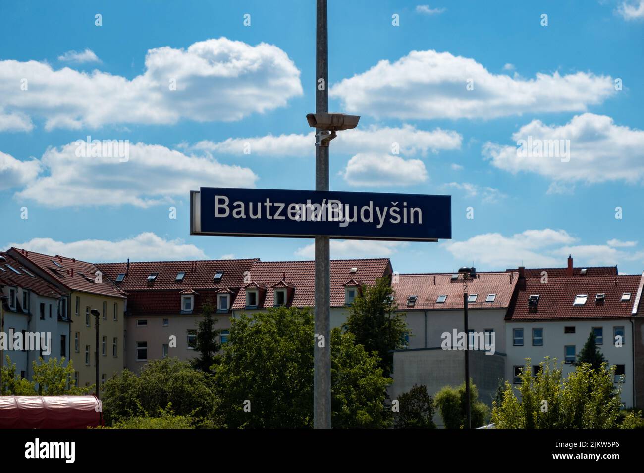 Bautzen cartello con il nome alla stazione ferroviaria. Lettere bianche su una piastra metallica blu montata su un palo con un altoparlante. Cartello d'ingresso alla fermata del treno. Foto Stock