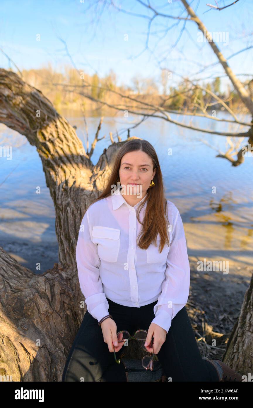 Una donna sicura all'aperto di fronte ad un fiume si siede su un ramo di albero Foto Stock