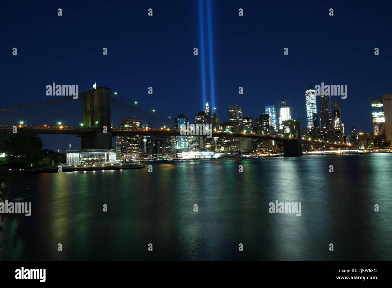 Uno scenario notturno del Ponte di Brooklyn e dello skyline di New York con due linee di luci al neon dalla baia Foto Stock