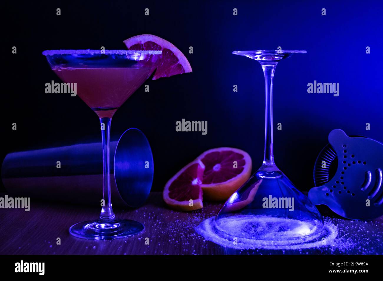 Un primo piano di due bicchieri martini con zucchero e cocktail di pompelmo sotto la luce blu del club Foto Stock