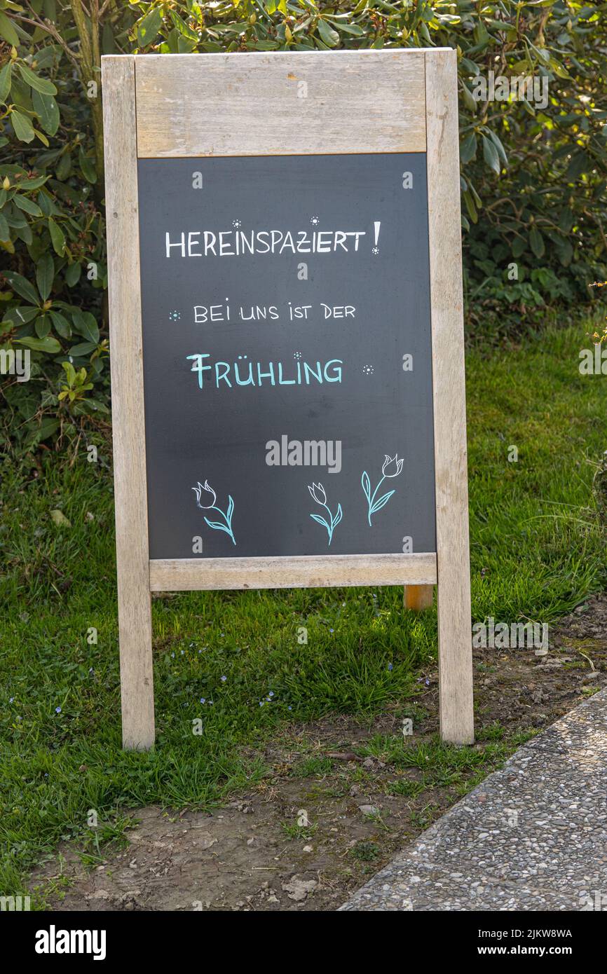 Una tavola di legno all'aperto con scritta ''come in, there is spring'' in tedesco Foto Stock