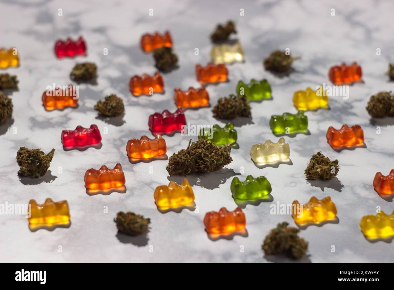 Diversi germogli secchi di marijuana medica giacciono in ordine tra orsacchiotti di colori diversi con l'aggiunta di olio cbd su un tavolo di marmo, che costituisce un p Foto Stock