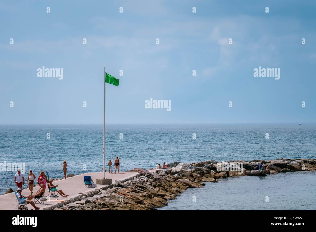 Interruttore di lunghezza d'onda di piccole dimensioni con indicatore verde, che indica condizioni di sicurezza del mare. Le persone camminano e abbronzano sotto l'estate Sun, MARBELLA, MALAGA/SPAGNA - LUGLIO 21 2022 Foto Stock