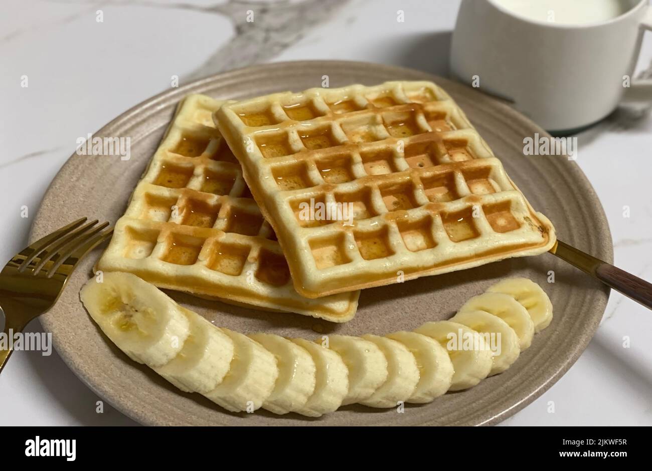 Un primo piano di un piatto con deliziosi waffle dolci con guarnizione di sciroppo d'acero e banane a fette Foto Stock