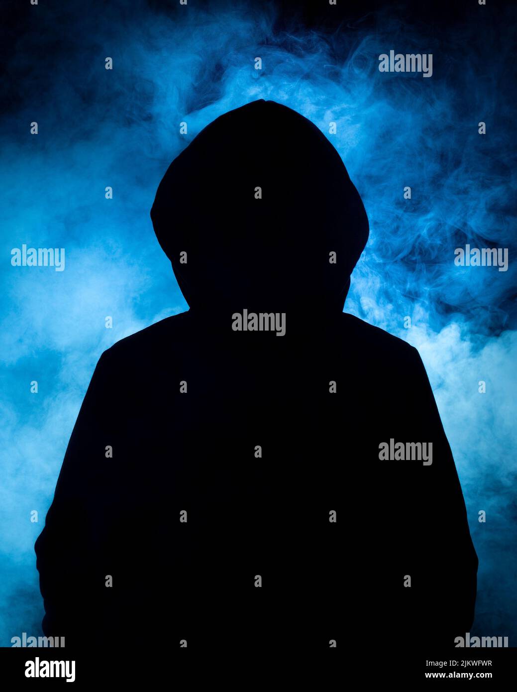 Un colpo verticale di un uomo con una parte superiore nera scura con uno sfondo di fumo blu, concetti cybercriminali Foto Stock