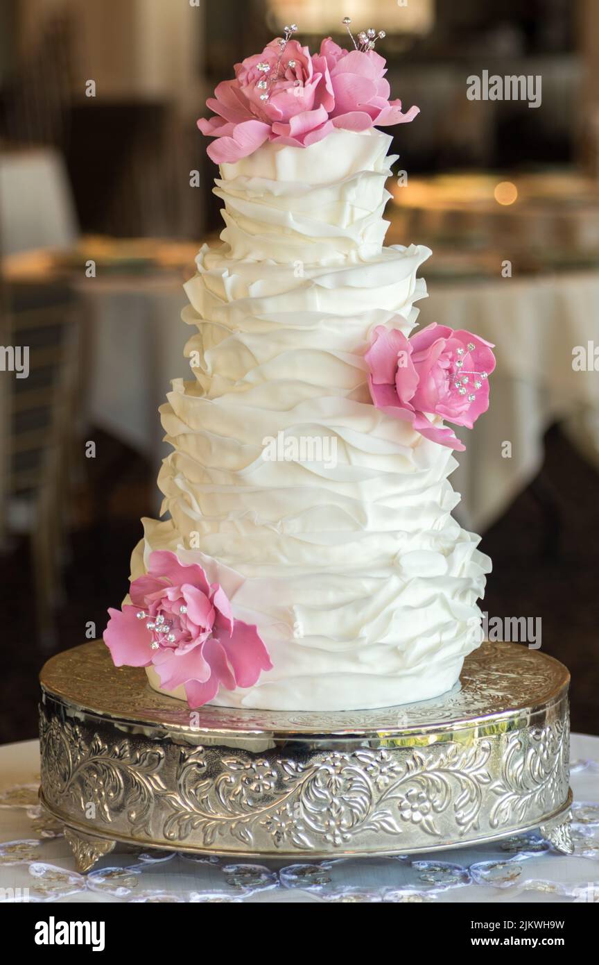 Una torta di nozze con volant bianco con fiori commestibili Foto Stock