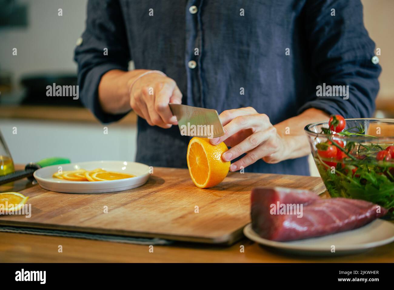 Un primo piano dell'uomo che taglia l'arancia sul legno in cucina. Concetto di cucina. Foto Stock