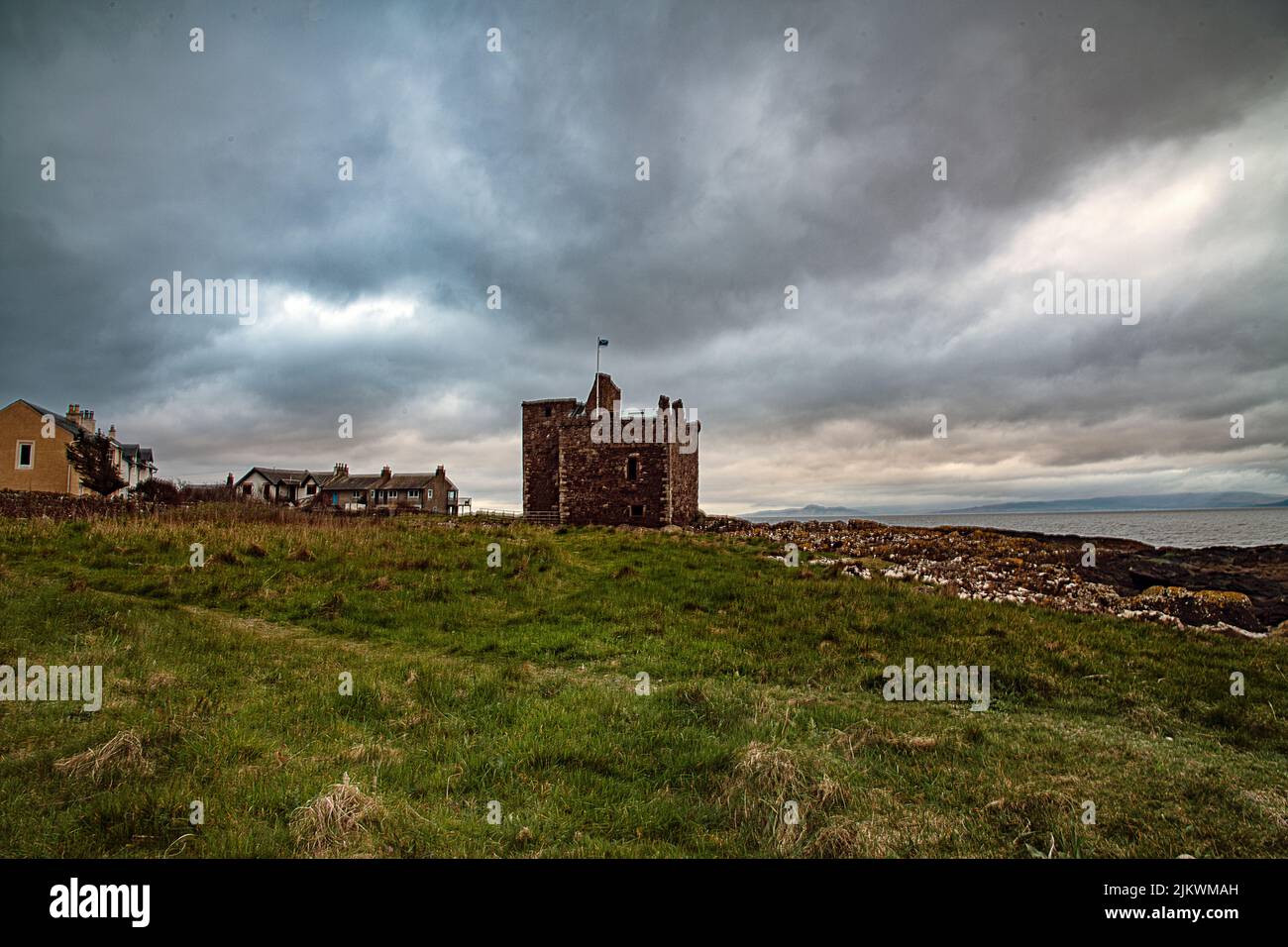 Una bella vista sul vecchio castello di Portencross con una bandiera in cima di fronte all'acqua Foto Stock