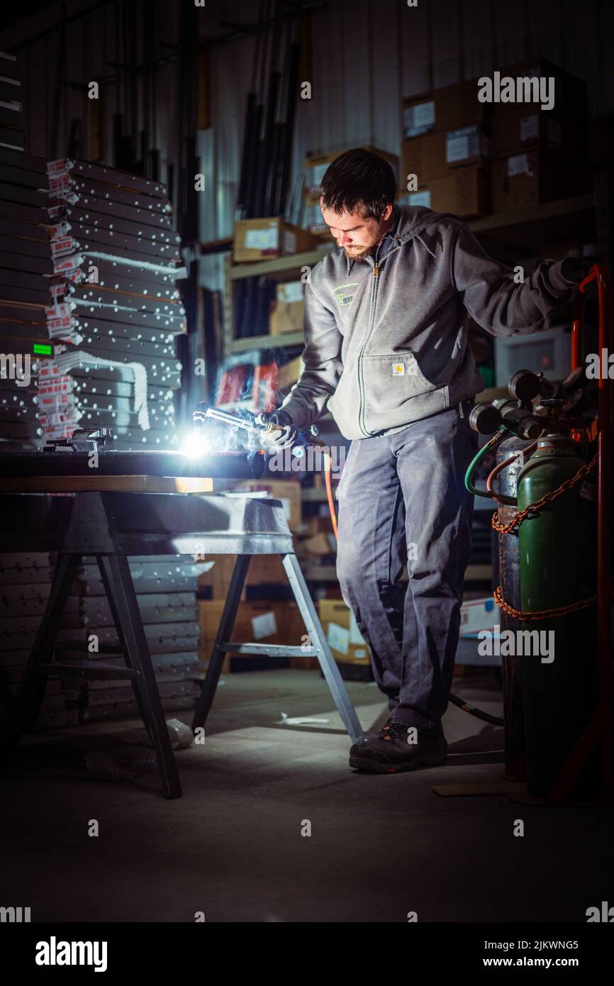 Un colpo verticale di un uomo con una torcia da taglio, gettando le ombre via con una fiamma luminosa Foto Stock