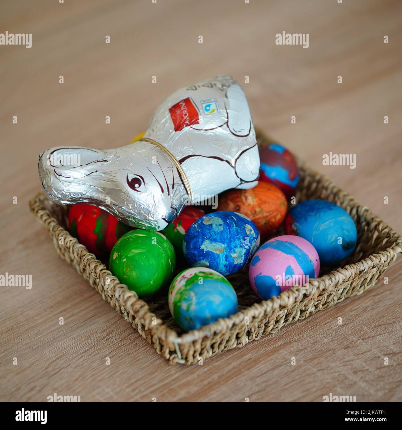 Un primo piano di un colorato dipinto uova di pasqua e coniglietto di cioccolato in un cesto di paglia su un tavolo di legno Foto Stock