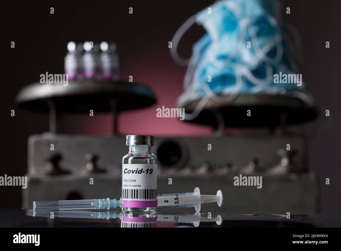 Primo piano di quattro fiale di vaccino ANTICOVID con siringa e maschere chirurgiche. Sullo sfondo una vecchia scala Foto Stock