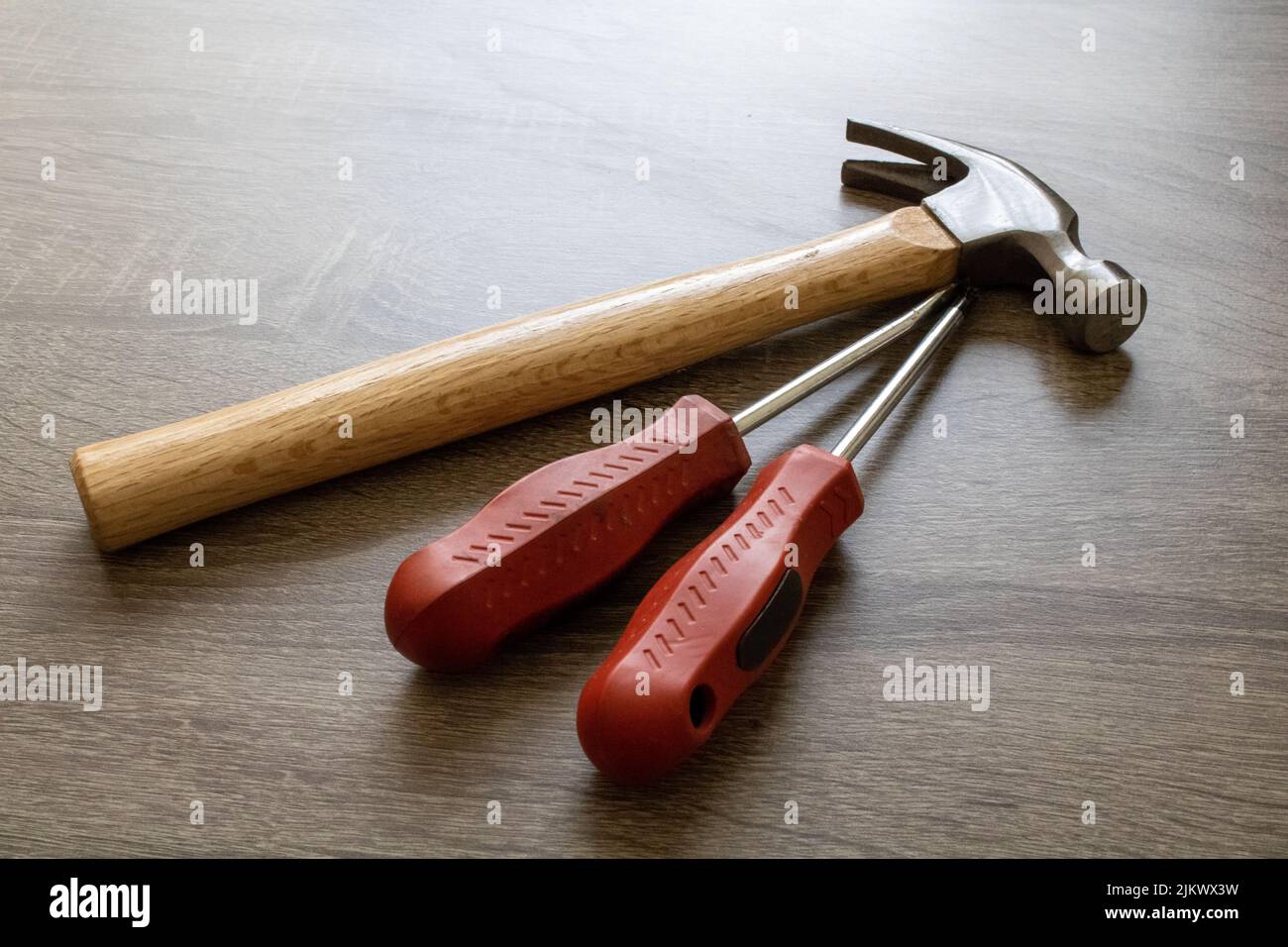 Un primo piano di un martello di legno con due cacciaviti rossi su un tavolo Foto Stock