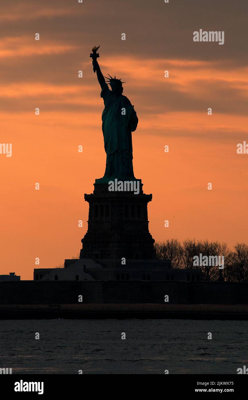 Silhouette della Statua della libertà contro un vivace concetto di cielo arancione al tramonto per i monumenti di New York, il patriottismo americano e simbolo della libertà in America Foto Stock