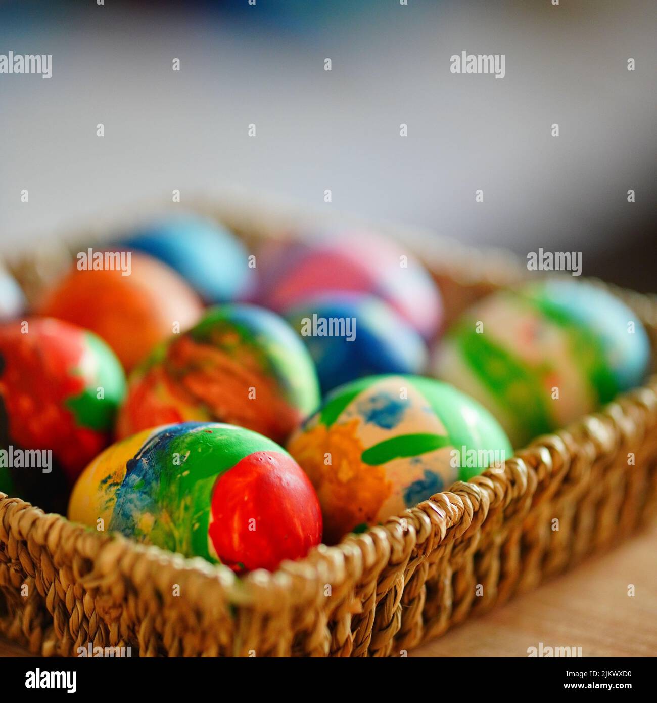 Un primo piano di un colorato dipinto uova di pasqua in cesto di paglia su un tavolo di legno Foto Stock