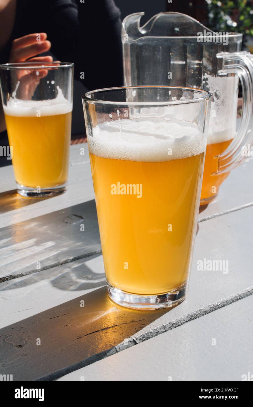 due bicchieri di birra sul tavolo all'aperto con caraffa di birra e mano Foto Stock