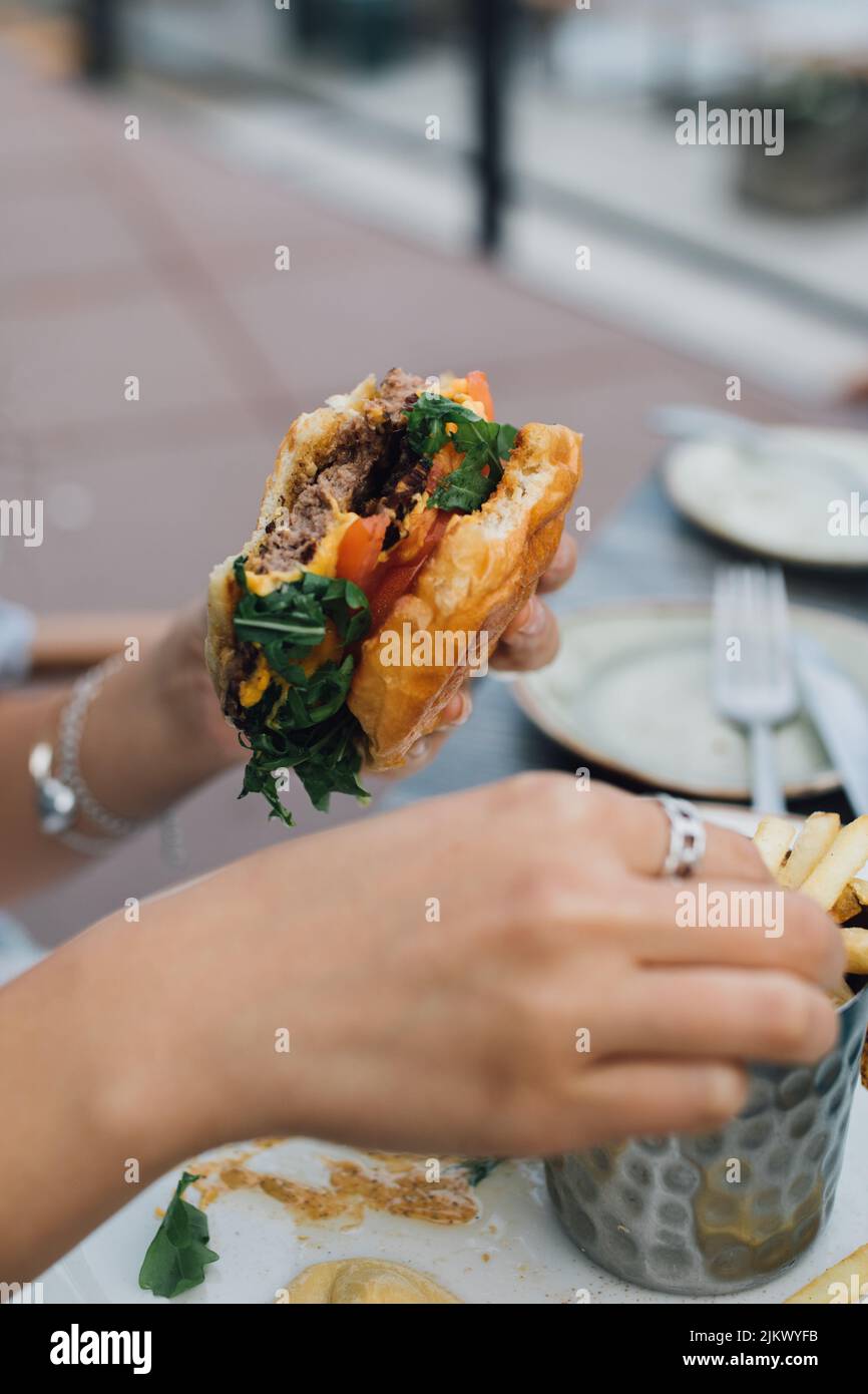 Donna che tiene metà mangiato hamburger in una mano e mangiare patatine fritte con l'altra mano Foto Stock