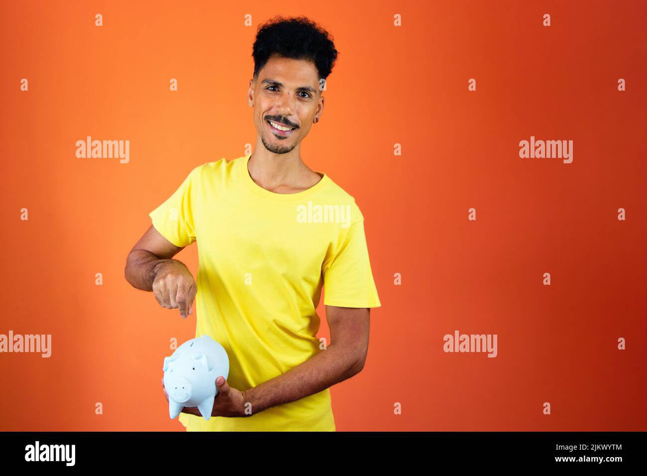 Bell'uomo nero che tiene una Piggy Bank isolato su Orange. Foto Stock