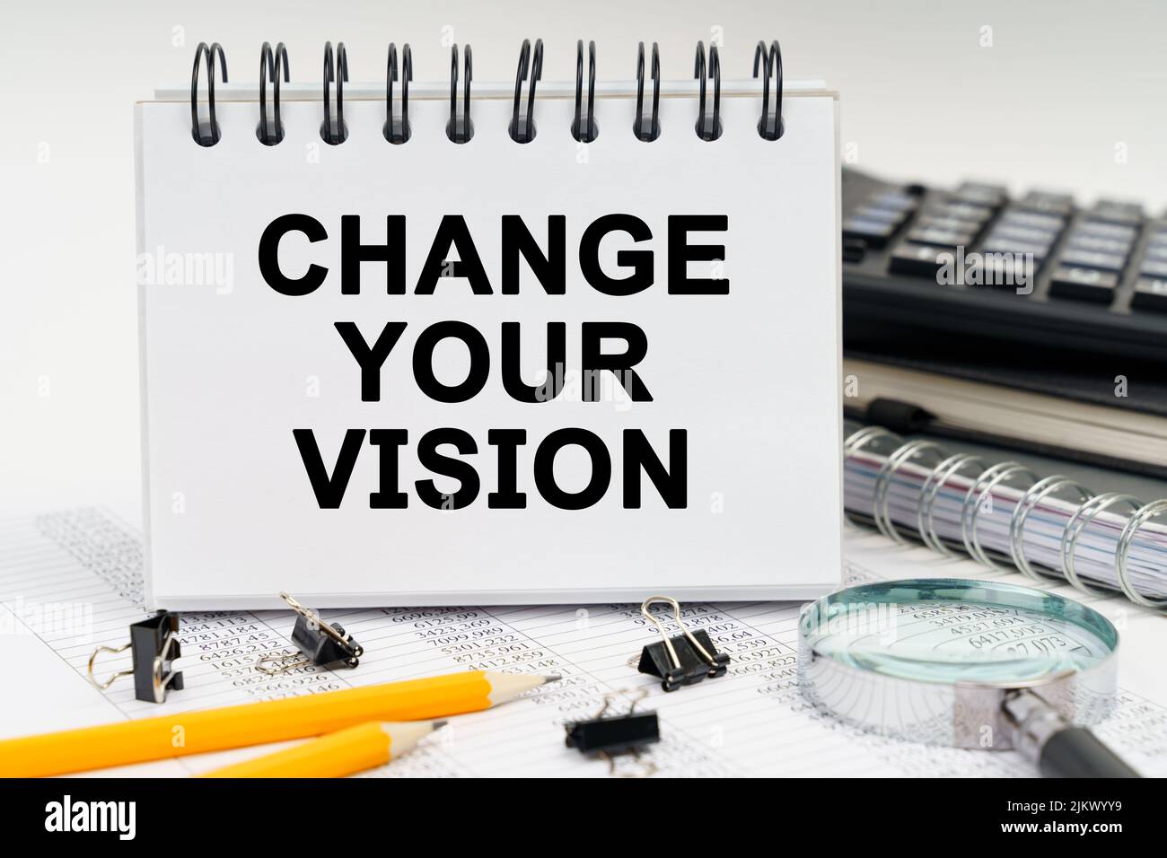 Concetto di economia e business. Sul tavolo c'è una lente d'ingrandimento, matite, diari e un quaderno con l'iscrizione - CAMBIARE LA VOSTRA VISIONE Foto Stock