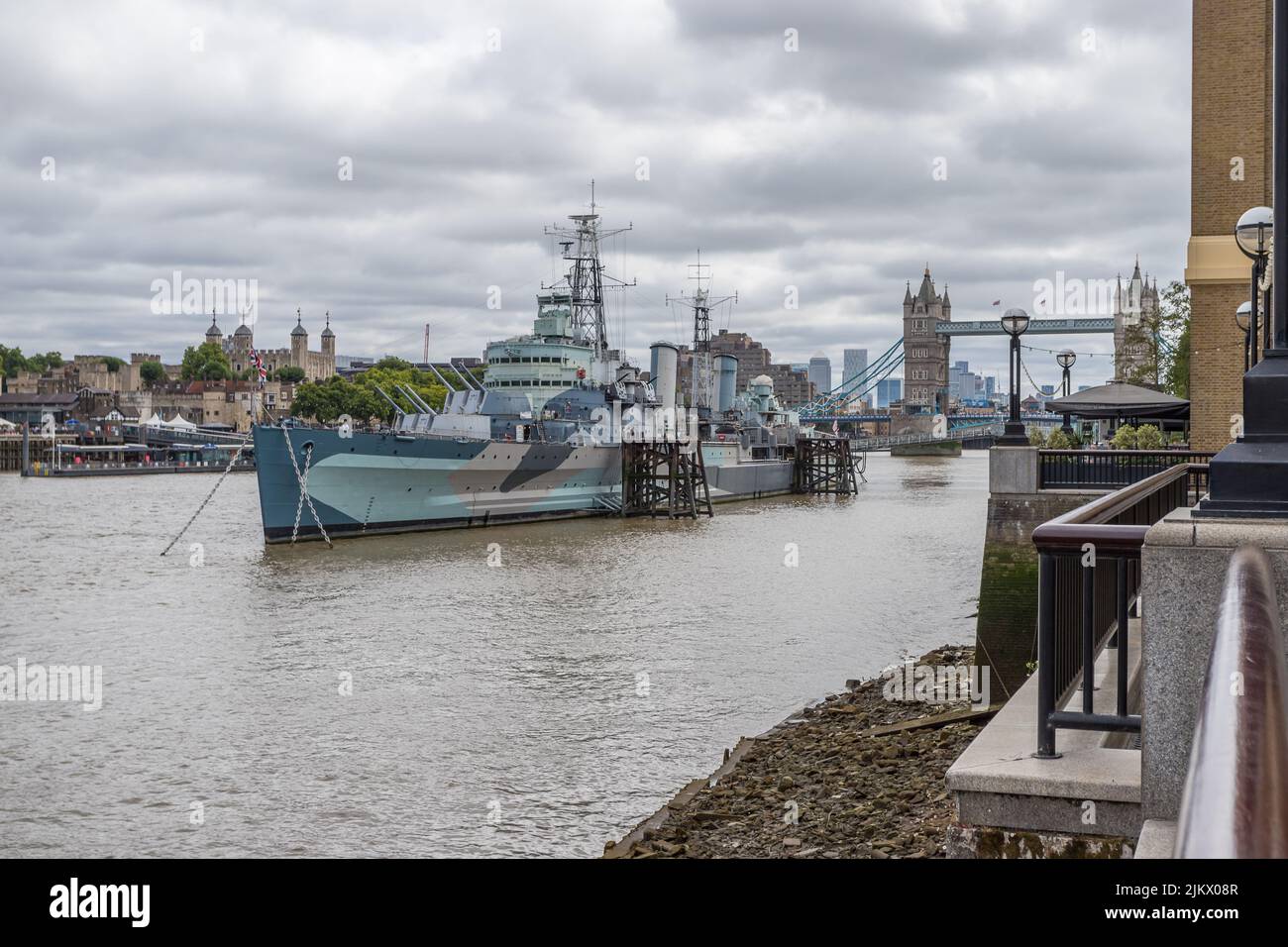 HMS Belfast catturato dalla Queens Walk a Londra nell'agosto 2022. La Torre di Londra, il Tower Bridge e Canary Wharf possono essere visti dietro la barca mu Foto Stock