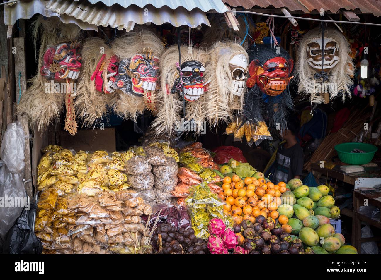 Un gruppo di maschere spaventose e frutta assortita esposte in un mercato balinese in Indonesia Foto Stock