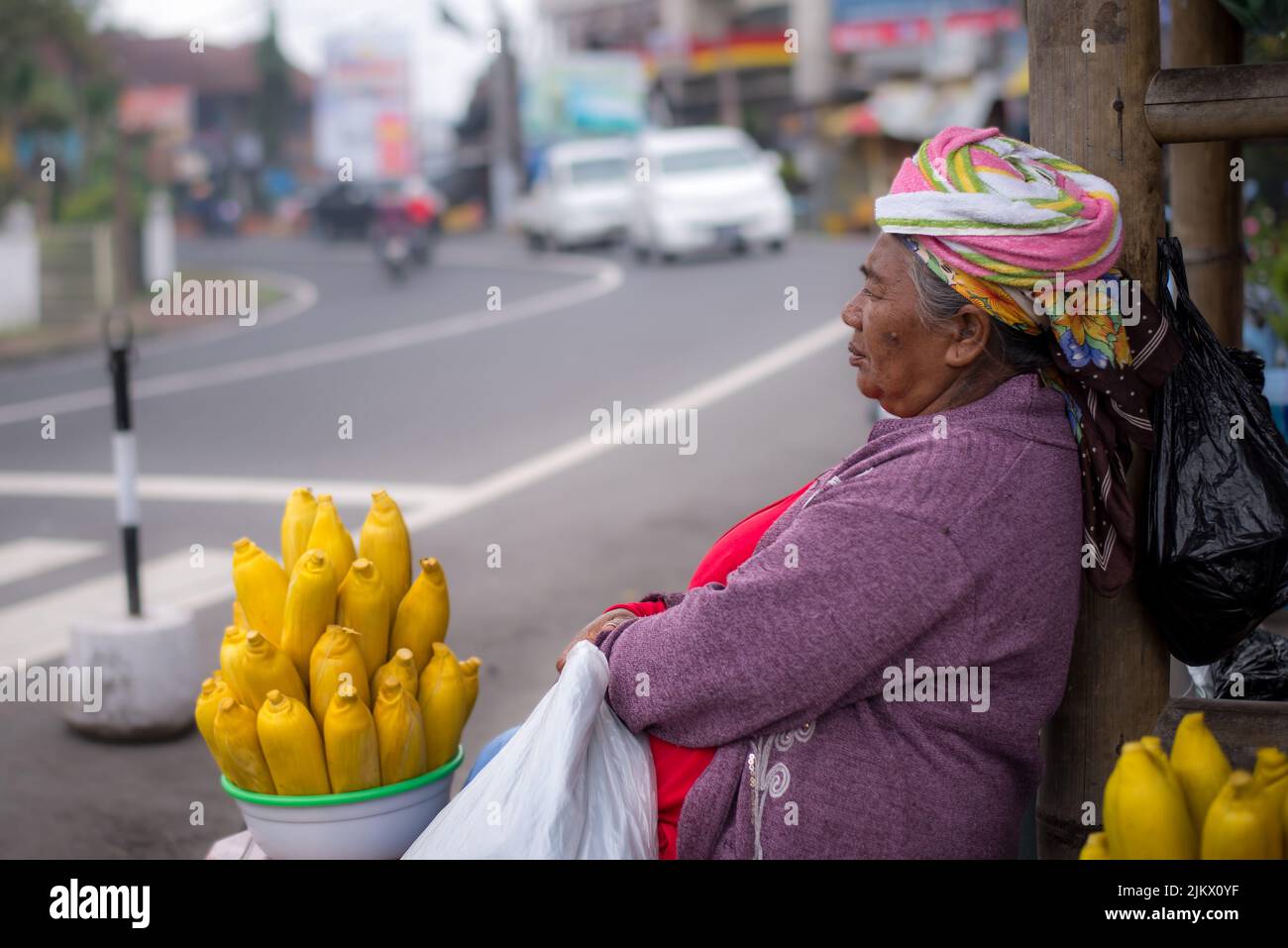 Un primo piano di un'anziana signora Balinese in rosso che vende mais giallo brillante a Bali, Indonesia Foto Stock
